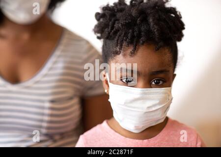 Madre afroamericana che aiuta la figlia a indossare una maschera facciale. Foto Stock