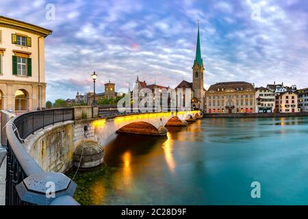 Famosa chiesa Fraumunster e ponte Munsterbrucke sul fiume Limmat al tramonto nel centro storico di Zurigo, la città più grande della Svizzera Foto Stock