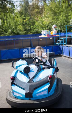 La bambina corre su macchinine elettriche giocattolo blu nel parco Foto Stock