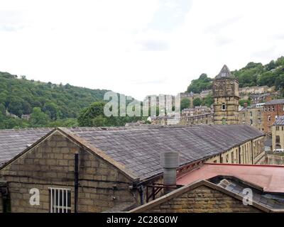 una vista sulle ripide strade collinari del ponte di hebden tra alberi estivi con la torre dello storico mulino di noce comune Foto Stock