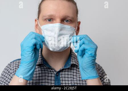 Guy mette sulla maschera respiratoria. L'uomo attraente mette sulla maschera del viso e guarda la macchina fotografica. Raffreddore, influenza, virus, tonsillite, malattie respiratorie acute, quaranti Foto Stock