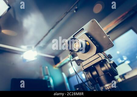 Videocamera cinematografica moderna su un treppiede in uno studio di trasmissione, faretti e altre attrezzature Foto Stock