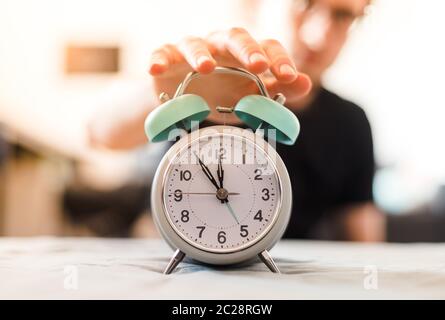 L'uomo sta premendo una sveglia al mattino, sole e sfondo sfocato Foto Stock