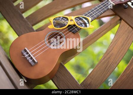 Estate: Ukulele con occhiali da sole gialli su una panchina di legno del parco Foto Stock