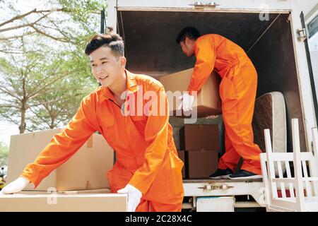 Due giovani uomini adulti che indossano abiti uniformi arancioni caricando camion con oggetti domestici Foto Stock