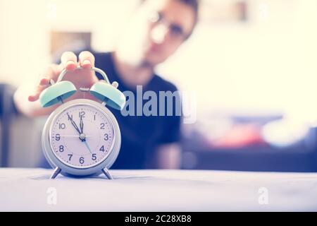 L'uomo sta premendo una sveglia al mattino, sole e sfondo sfocato Foto Stock