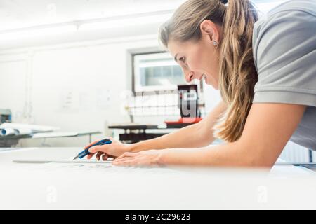 Donna segni di taglio o vinil avvolge la produzione di materiale pubblicitario in officina di agenzia Foto Stock