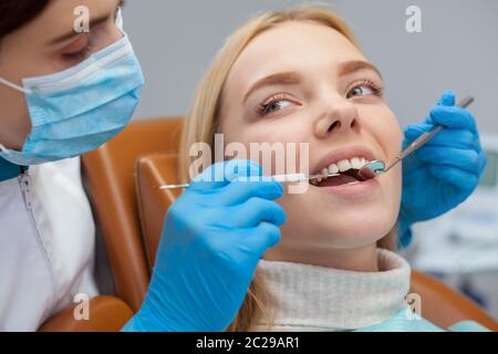 Primo piano di una bella giovane donna che guarda rilassato e felice mentre ottiene i suoi denti esaminati da dentista professionista. Ripresa tagliata di una femmina Foto Stock
