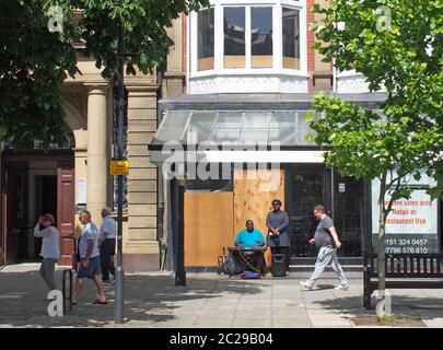 un uomo e una donna che suonano l'organo e cantano fuori da un negozio vuoto su lord street a southport merseyside con persone che camminano p Foto Stock