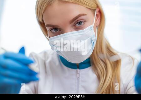 Primo piano di una dottoressa che si avvicina alla fotocamera con strumenti medici in mano. Dentista femminile che indossa maschera medica pronto per esaminare il vostro Foto Stock