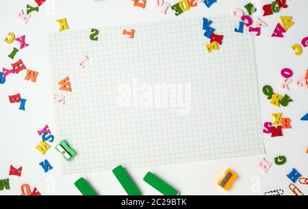 Fogli bianchi in una gabbia e piccole multi-colore lettere in legno, torna a scuola, spazio di copia Foto Stock