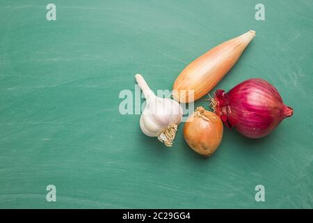 Il golden scalogno cipolla e aglio. Le lampadine di fresco sulla lavagna verde. Vista dall'alto. Foto Stock