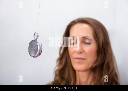 Attraente donna matura essendo ipnotizzato con pendolo a casa Foto Stock
