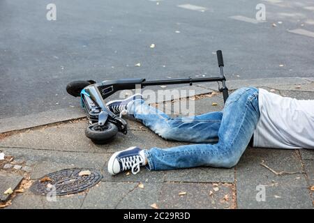 Inconscio uomo disteso sul cemento Street dopo un incidente con uno scooter elettrico Foto Stock