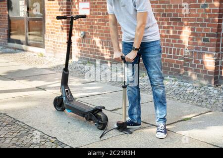 L'uomo il pompaggio di aria nel pneumatico sul suo E-scooter Foto Stock