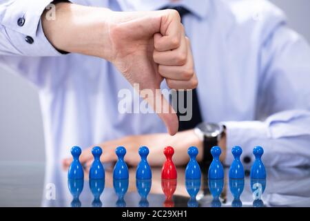 Discriminazione sul posto di lavoro concetto. La mano che mostra il pollice verso il basso vicino a pedina rossa Foto Stock