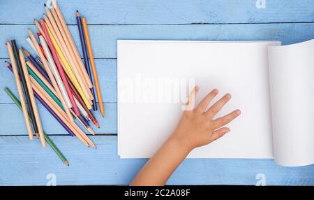 I bambini con le mani in mano a disegnare con le matite in album sul tavolo blu Foto Stock