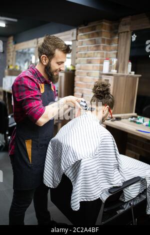 Giovane uomo bearded ottenere capelli dal parrucchiere con rasoio elettrico al barbiere Foto Stock