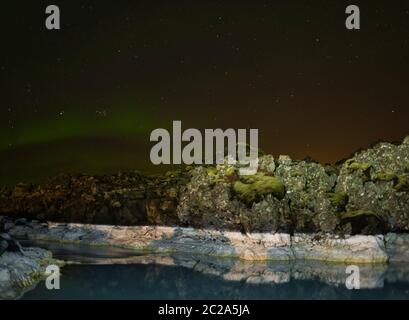 Luci del nord e riflettendo le rocce in acqua termale Foto Stock