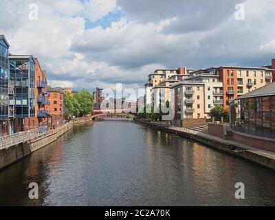 una vista lungo il fiume aire a leeds con appartamenti e edifici sul mare con ponte a corona in lontananza Foto Stock