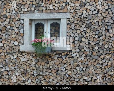 Finestra divertente con decorazione floreale in un muro di legna da ardere Foto Stock
