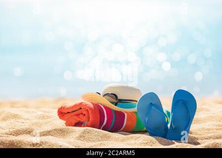 Accessori spiaggia cappello di paglia, infradito, asciugamano sulla soleggiata spiaggia tropicale, vacanze estive Foto Stock