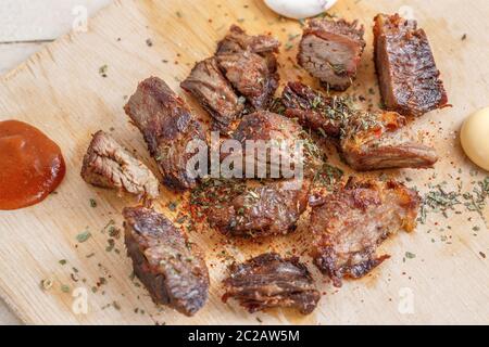 Pezzi di carne arrosto con spezie su un vassoio di legno con quattro tipi di salse a base di carne Foto Stock