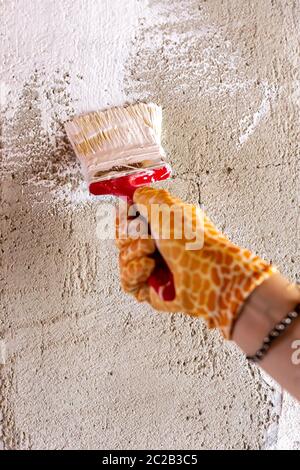 Verniciare una parete di cemento con vernice bianca utilizzando una spazzola. Guanti gialli con motivo giraffa. Foto Stock