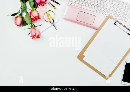 Elegante struttura a cornice piatta con notebook rosa, rose e altri accessori su bianco. Mockup di affari femminile, copyspace Foto Stock