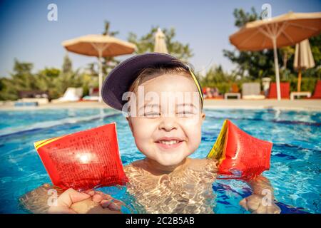 Un piccolo ragazzo impara a nuotare in piscina in estate con il sostegno di suo padre le mani Foto Stock