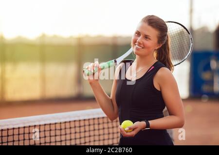 Giocatore di tennis. Sorridenti girl, in piedi con la racchetta e la palla da tennis sulla corte, nei pressi del net, guardando lontano. Sport concept. Foto Stock