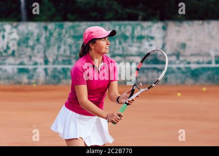 Giocatore di tennis. Attraente giovane donna giocando a tennis e in attesa per il servire. Vestito di t-shirt sportiva e mantello. All'esterno. Foto Stock