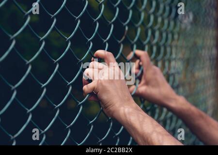 Mano di giovane uomo che tiene su recinzione di collegamento della catena per la libertà, la Giornata dei diritti umani, concetto di immigrato. Foto Stock