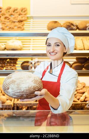 Commessa con grembiule presentando il pane fresco in un panificio che guardando nella telecamera Foto Stock