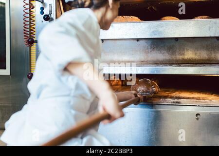 Baker mettendo il pane nel forno del pane accovacciata sul pavimento del forno Foto Stock