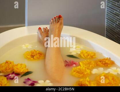 Giovane donna in bagno con latte e fiori Foto Stock