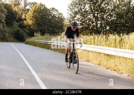 Ritratto a lunghezza intera del ciclista in bicicletta sportiva in bicicletta in bicicletta in modo dinamico durante le giornate di sole. Uomo maturo in casco e occhiali di formazione su aria fresca Foto Stock