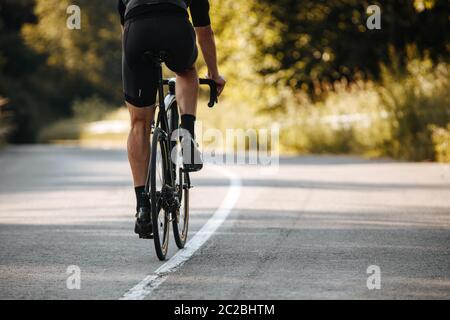 Indietro vista del ciclista in activewear bici professionale su strada asfaltata con sfondo sfocato di piante verdi. Concetto di stile di vita attivo e di t duro Foto Stock