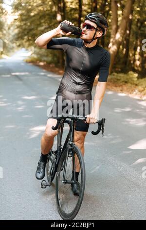 Ritratto di un uomo maturo in costume sportivo rinfrescante con acqua dopo una lunga percorrenza in bicicletta. Uomo forte in casco e occhiali da vista bere Foto Stock