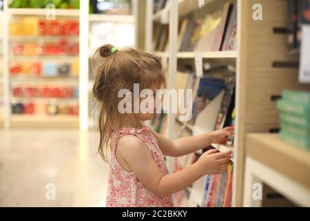 Piccolo bambino carino che raccoglie i libri dalla libreria Foto Stock