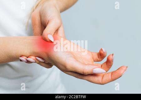 Closeup di braccia femminili che tengono il suo polso doloroso causato da un lavoro prolungato sul computer, laptop, colorato in rosso.Carpal tunnel sindrome, artrite, Foto Stock
