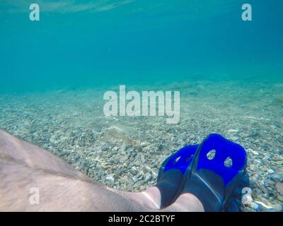 Foto subacquea delle gambe maschili con pinne blu. Foto Stock