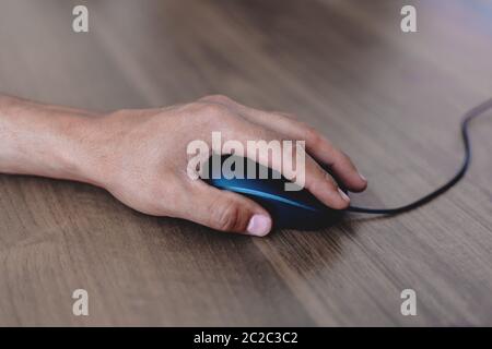 Un uomo usa un mouse di computer su un tavolo di legno. Foto Stock
