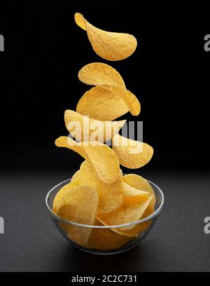 Potato chips di cadere nella ciotola di vetro su sfondo nero Foto Stock