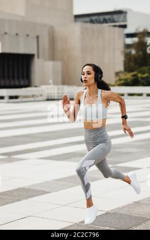 Sportiva che si springe in città. Donna in abbigliamento sportivo e cuffie che corrono velocemente all'aperto. Foto Stock