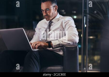 Uomo d'affari che lavora su un computer portatile mentre attende il suo volo nella sala dell'aeroporto. Uomo in uso computer portatile presso l'area di attesa aeroporto. Foto Stock