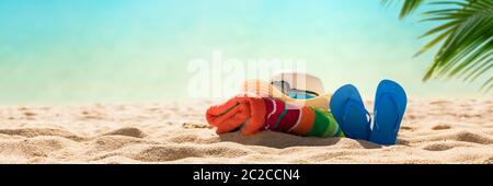 Accessori spiaggia cappello di paglia, infradito, asciugamano sulla soleggiata spiaggia tropicale, vacanze estive Foto Stock