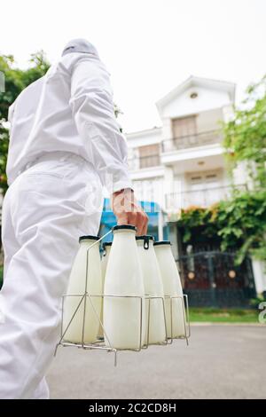 Uomo irriconoscibile che indossa una uniforme bianca per offrire latte fresco ai clienti, shot verticale ad angolo basso Foto Stock