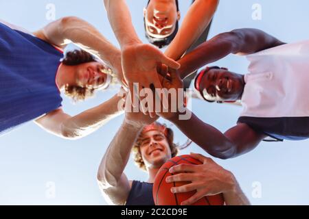 Vista dal basso di giovani sportivi con basket mettendo le mani insieme all'aperto Foto Stock