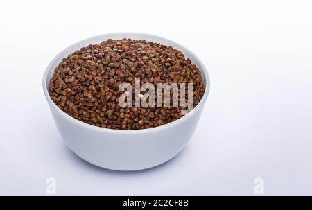 Semi di grano saraceno isolati su sfondo bianco, ceramica ciotola piena di chicchi di grano saraceno Foto Stock